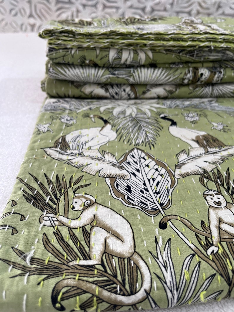 May include: A green kantha quilt with a white and brown floral pattern featuring monkeys and birds. The quilt is made of cotton and is hand-stitched.