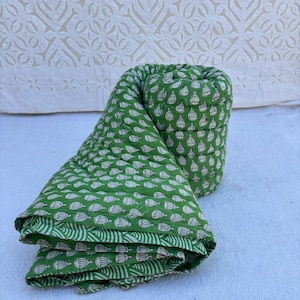 May include: A green cotton quilt with a white floral pattern. The quilt is rolled up and folded, showing the fabric's texture and design.