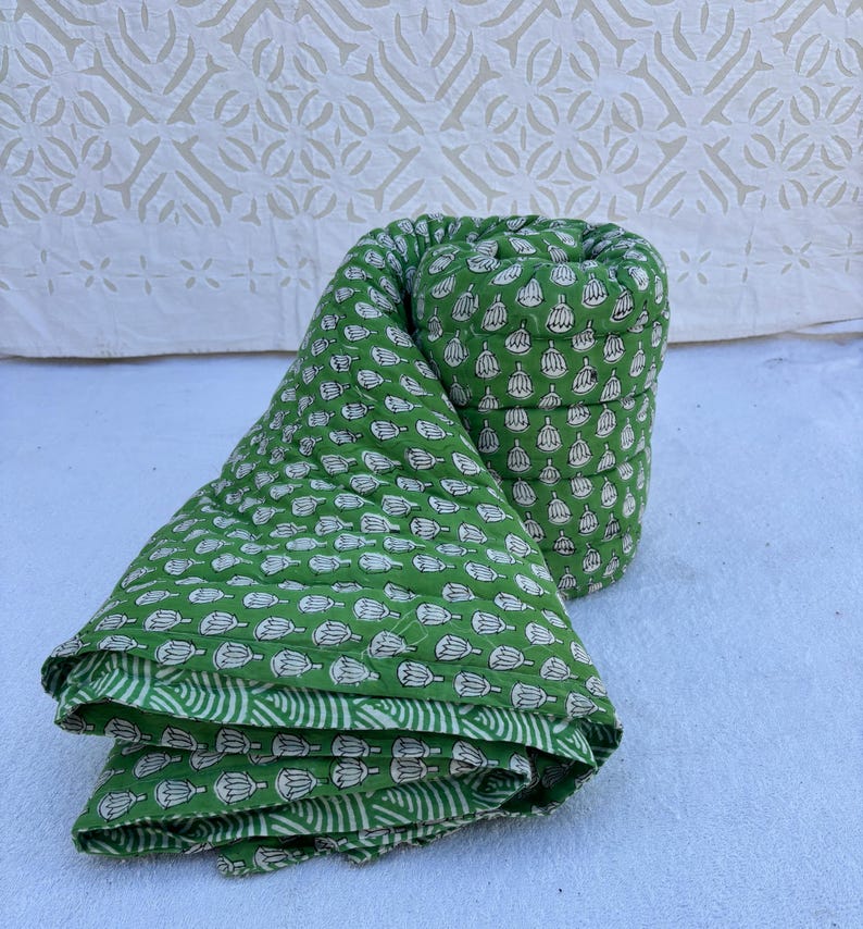 May include: A green cotton quilt with a white floral pattern. The quilt is rolled up and folded, showing the fabric's texture and design.