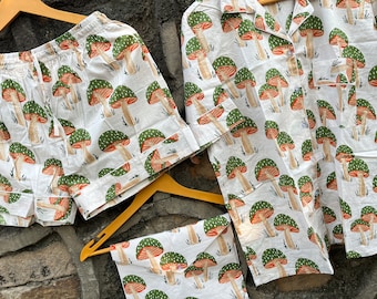 Puede incluir: Un conjunto de pijama blanco con estampado de setas verdes y naranjas. El conjunto incluye una camisa de manga corta y pantalones cortos.