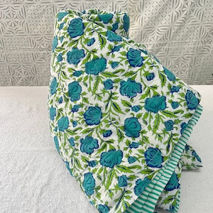 May include: A white cotton quilt with a blue and green floral print. The quilt is folded in half and has a green and white striped border.