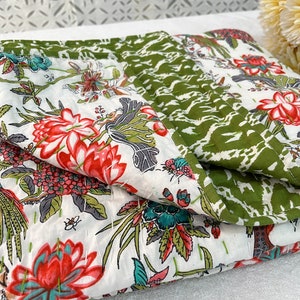 May include: A white and green floral patterned quilt with a white background and red, green, and blue flowers. The quilt is folded in half and the green side is visible.