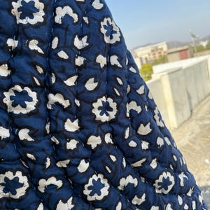 May include: A close-up of a blue quilted fabric with a white floral pattern. The fabric is textured and has a slightly raised design.