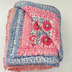 May include: A pink and blue floral patterned quilt folded in half. The quilt has a white background with pink and blue floral designs and a blue border.