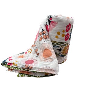 May include: A white muslin swaddle blanket with a floral print featuring pink, orange, yellow, and green flowers. The blanket is rolled up and has a white background.