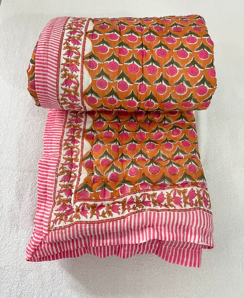 May include: A pink and orange cotton quilt with a floral print. The quilt has a white border with pink stripes and a pink and white striped border.