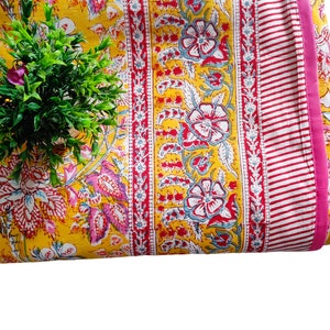 May include: Yellow fabric with a floral print in shades of pink, red, and blue. The fabric has a pink and white striped border.