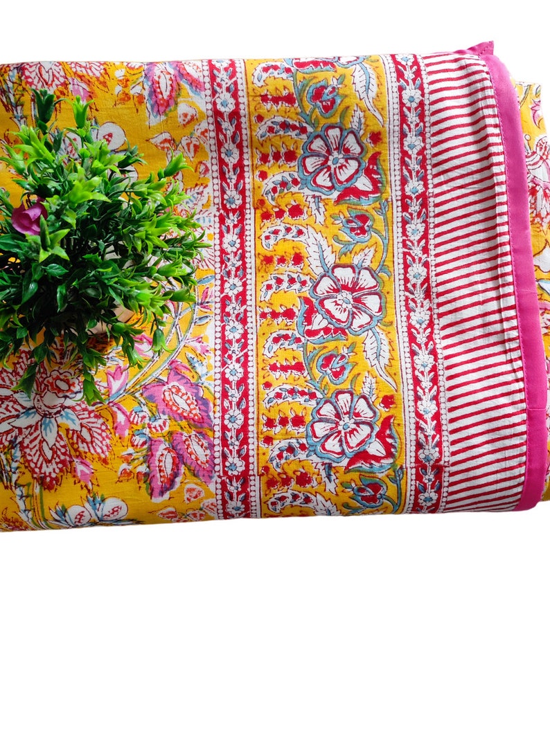 May include: Yellow fabric with a floral print in shades of pink, red, and blue. The fabric has a pink and white striped border.