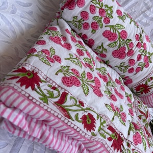 May include: White and pink floral patterned quilt and pillow set. The quilt features a repeating pattern of pink flowers and green leaves on a white background. The border has a pink and white striped design.