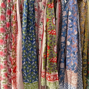 May include: A collection of colorful cotton scarves with various floral and geometric patterns. The scarves are hanging on a rack and are ready to be worn.