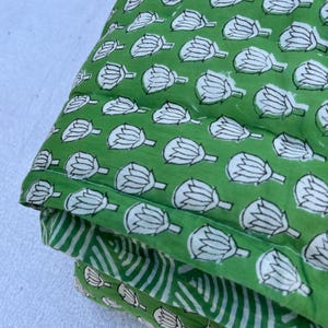 May include: A green and white cotton quilt with a floral pattern. The quilt is folded in thirds and has a white background.