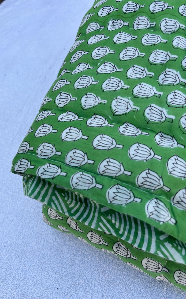 May include: A green and white cotton quilt with a floral pattern. The quilt is folded in thirds and has a white background.