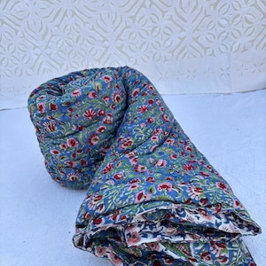 May include: A blue and pink floral patterned quilt is folded and rolled up. The quilt is made of cotton and has a soft, comfortable feel.