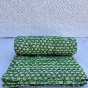 May include: A green cotton quilt with a white floral pattern. The quilt is folded in half and the top layer is rolled up.