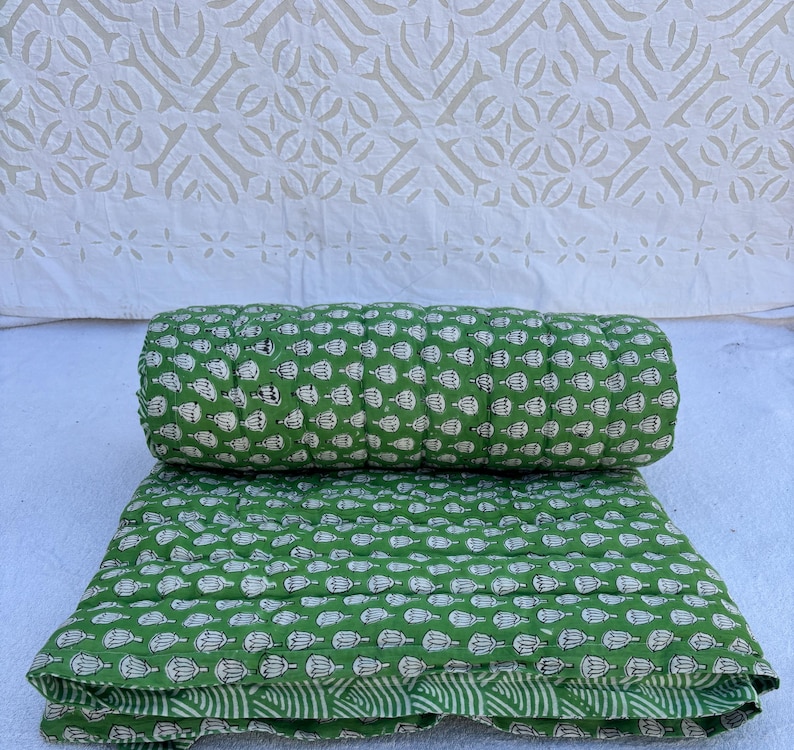 May include: A green cotton quilt with a white floral pattern. The quilt is folded in half and the top layer is rolled up.