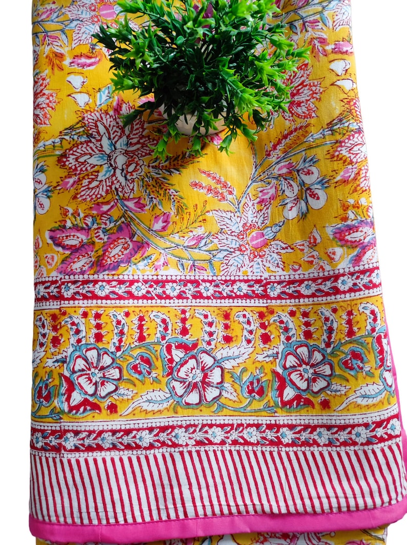 May include: A yellow cotton quilt with a pink floral pattern. The quilt has a pink border and a white and red striped border.