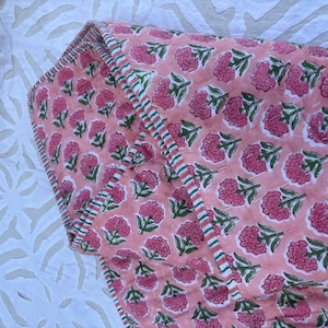 May include: Pink cotton quilt with a floral print and a green and white striped border.