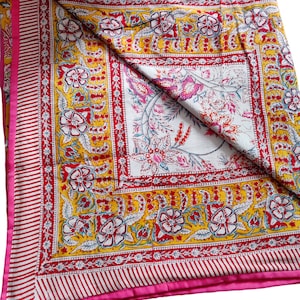 May include: A yellow and pink floral patterned quilt with a white center square. The quilt has a pink border with white stripes.