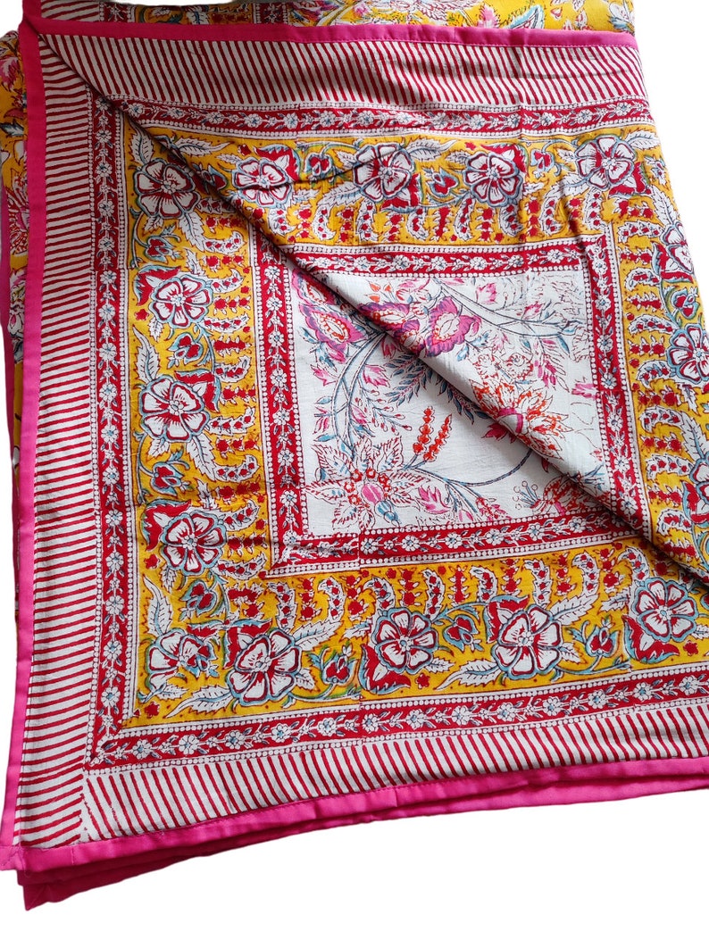 May include: A yellow and pink floral patterned quilt with a white center square. The quilt has a pink border with white stripes.