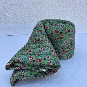 Op de afbeelding: Een groene en rode quilt met bloemenpatroon is opgerold en gevouwen op een wit oppervlak. De quilt is gemaakt van katoen en heeft een traditioneel Indiaas ontwerp.
