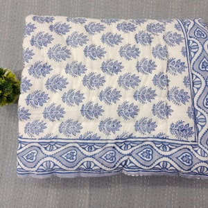 May include: White cotton quilt with a blue floral pattern and a blue border. The quilt is folded in half and has a white background.