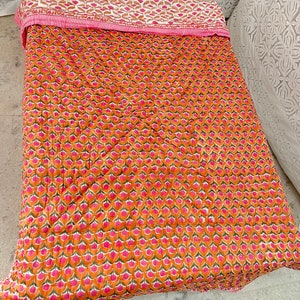 May include: A pink and orange kantha quilt with a floral pattern. The quilt is made of cotton and is hand-stitched.