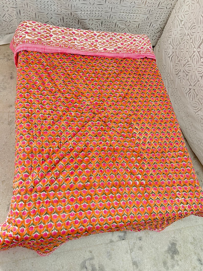 May include: A pink and orange kantha quilt with a floral pattern. The quilt is made of cotton and is hand-stitched.
