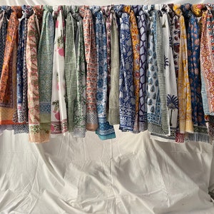 May include: A collection of colorful cotton scarves with various floral and geometric patterns hanging on a rack. The scarves are all different colors and designs, and they are all made of cotton.