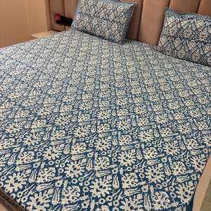 Peut inclure: Un ensemble de literie à motifs bleus et blancs, comprenant un drap-housse et deux taies d'oreiller. Le motif floral est répété sur la literie. La tête de lit est de couleur marron clair.