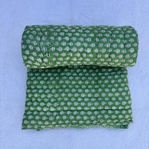 May include: A green and white kantha quilt with a floral pattern. The quilt is rolled up and folded in half.