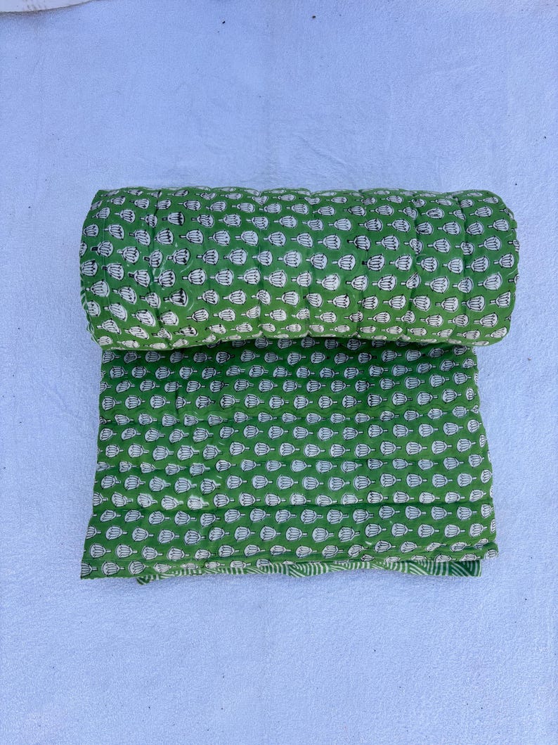 May include: A green and white kantha quilt with a floral pattern. The quilt is rolled up and folded in half.