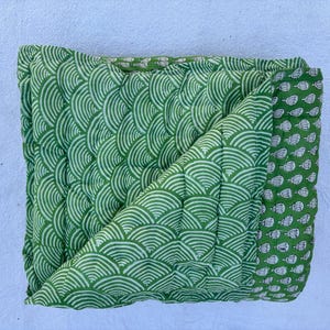 May include: A green and white quilted throw blanket with a wave pattern. The blanket is folded in half and has a border with a smaller pattern.