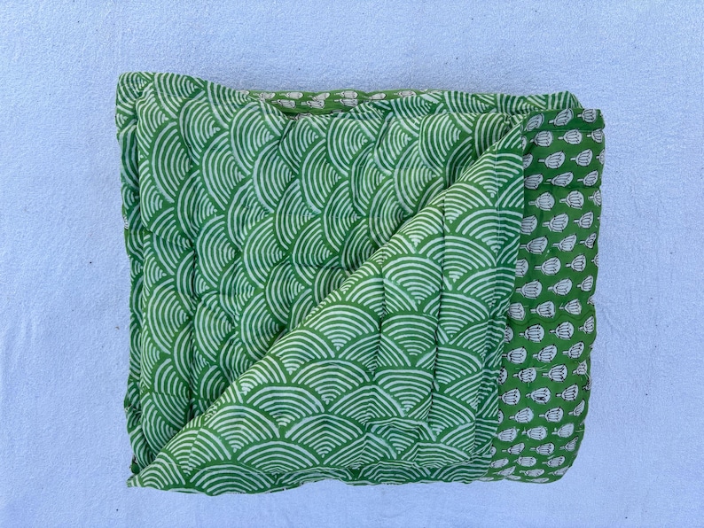 May include: A green and white quilted throw blanket with a wave pattern. The blanket is folded in half and has a border with a smaller pattern.