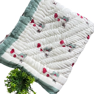 May include: White quilted baby blanket with a green border and a pattern of elephants holding pink balloons.