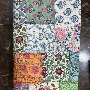 May include: A patchwork quilt featuring a range of floral patterns in shades of blue, green, pink, and orange. The quilt is made from cotton fabric and is quilted with a running stitch.