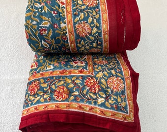 May include: A red and blue floral patterned quilt folded on a white surface. The quilt has a red border and a blue and white floral pattern.
