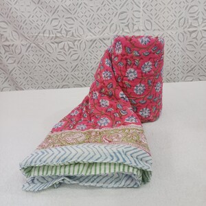 May include: A pink and green cotton quilt with a floral print. The quilt is rolled up and has a white background.