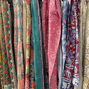 May include: A collection of colorful cotton scarves with floral and paisley patterns. The scarves are hanging on a rack and are ready to be purchased.