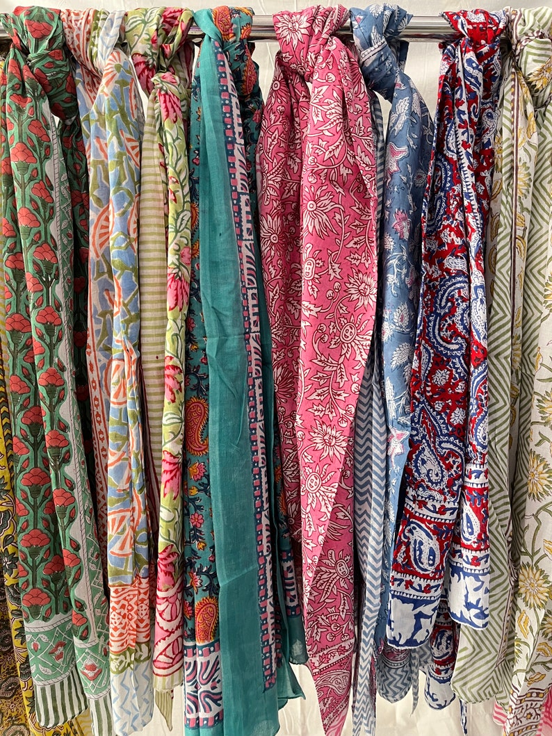 May include: A collection of colorful cotton scarves with floral and paisley patterns. The scarves are hanging on a rack and are ready to be purchased.