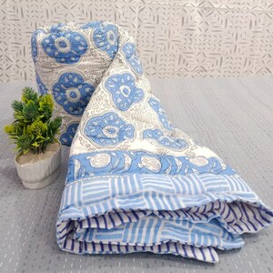 May include: A blue and white cotton quilt with a floral pattern. The quilt is folded and has a striped border.