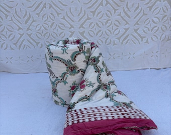May include: A white cotton quilt with a floral print in shades of green, pink, and brown. The quilt is rolled up and has a pink border.