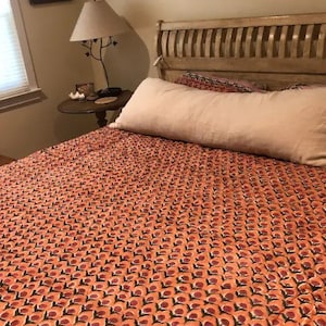 May include: A bed with a peach-colored patterned duvet cover and a white bolster pillow. The bed has a wooden headboard with vertical slats.