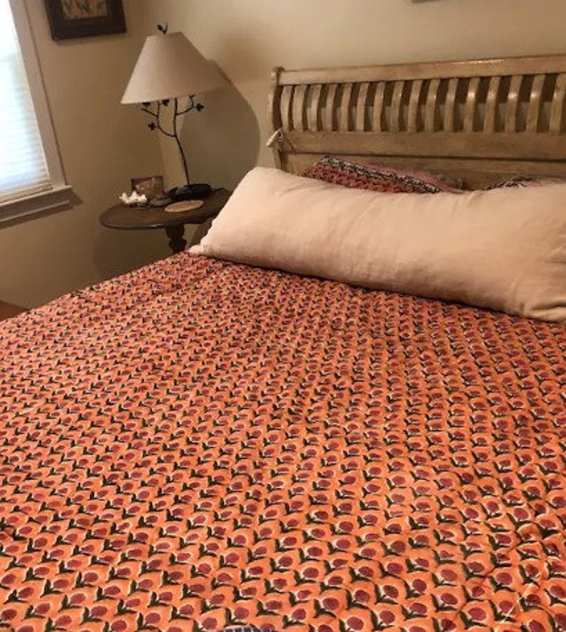 May include: A bed with a peach-colored patterned duvet cover and a white bolster pillow. The bed has a wooden headboard with vertical slats.