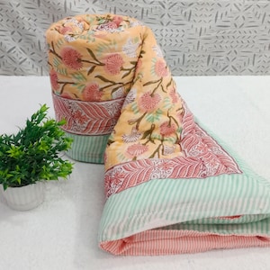 May include: A rolled up peach and green floral patterned cotton quilt with a white background. The quilt has a pink and green striped border.