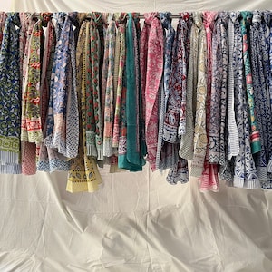 May include: A collection of colorful printed scarves hanging on a rack. The scarves are made of cotton and have a variety of patterns, including floral, geometric, and paisley.