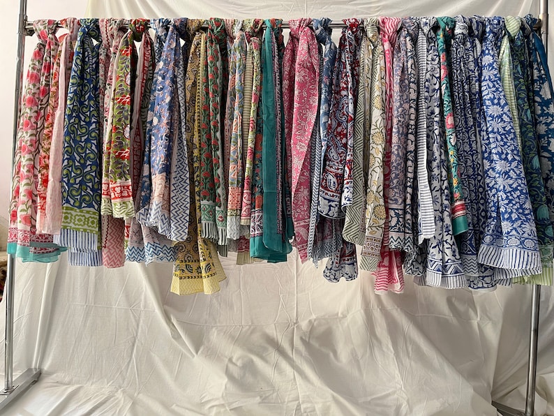 May include: A collection of colorful printed scarves hanging on a rack. The scarves are made of cotton and have a variety of patterns, including floral, geometric, and paisley.