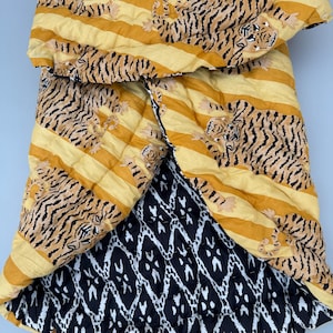 May include: A yellow and black quilted throw blanket with a tiger print on one side and a black and white geometric pattern on the other side.