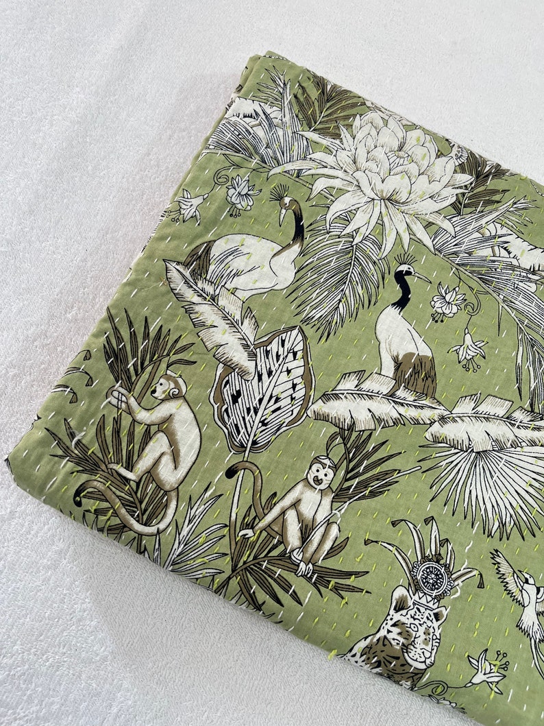 May include: A green kantha quilt with a jungle print featuring monkeys, birds, and a tiger. The quilt has a white background with black outlines and yellow stitching.