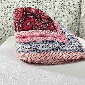 May include: A pink and red floral patterned quilt with blue and white trim. The quilt is folded and sitting on a white surface.