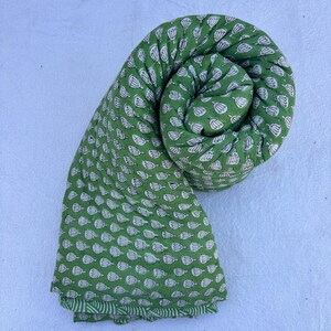 May include: A green cotton fabric with a white floral print. The fabric is rolled up into a spiral shape.